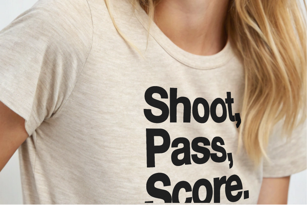 Woman wearing a t-shirt with 'Shoot, Pass, Score.' text on a plain background